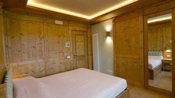 Habitación con paneles de madera, una cama, un radiador y un espejo que refleja el espacio.