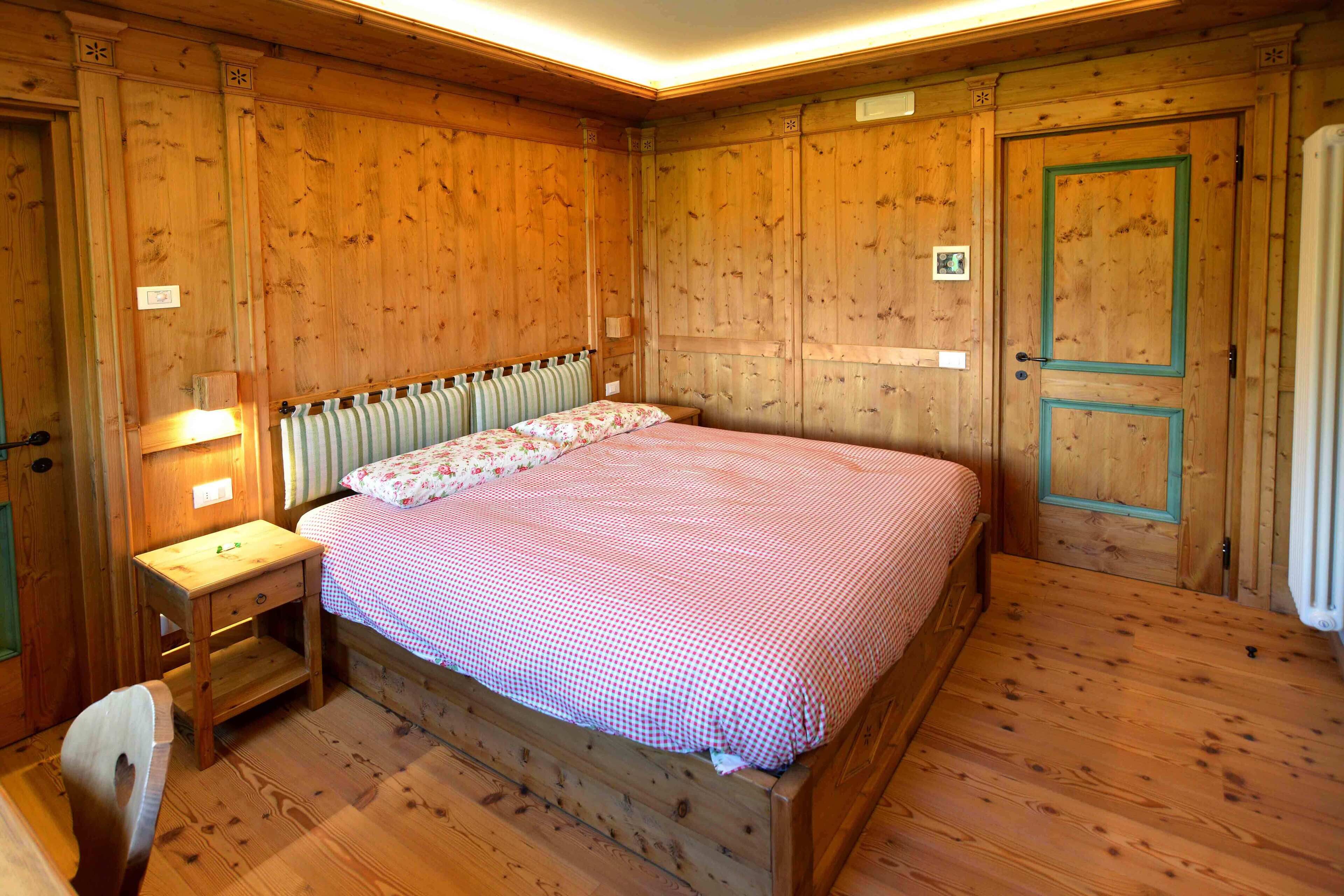 A wooden room with a bed, a nightstand, and a door.
