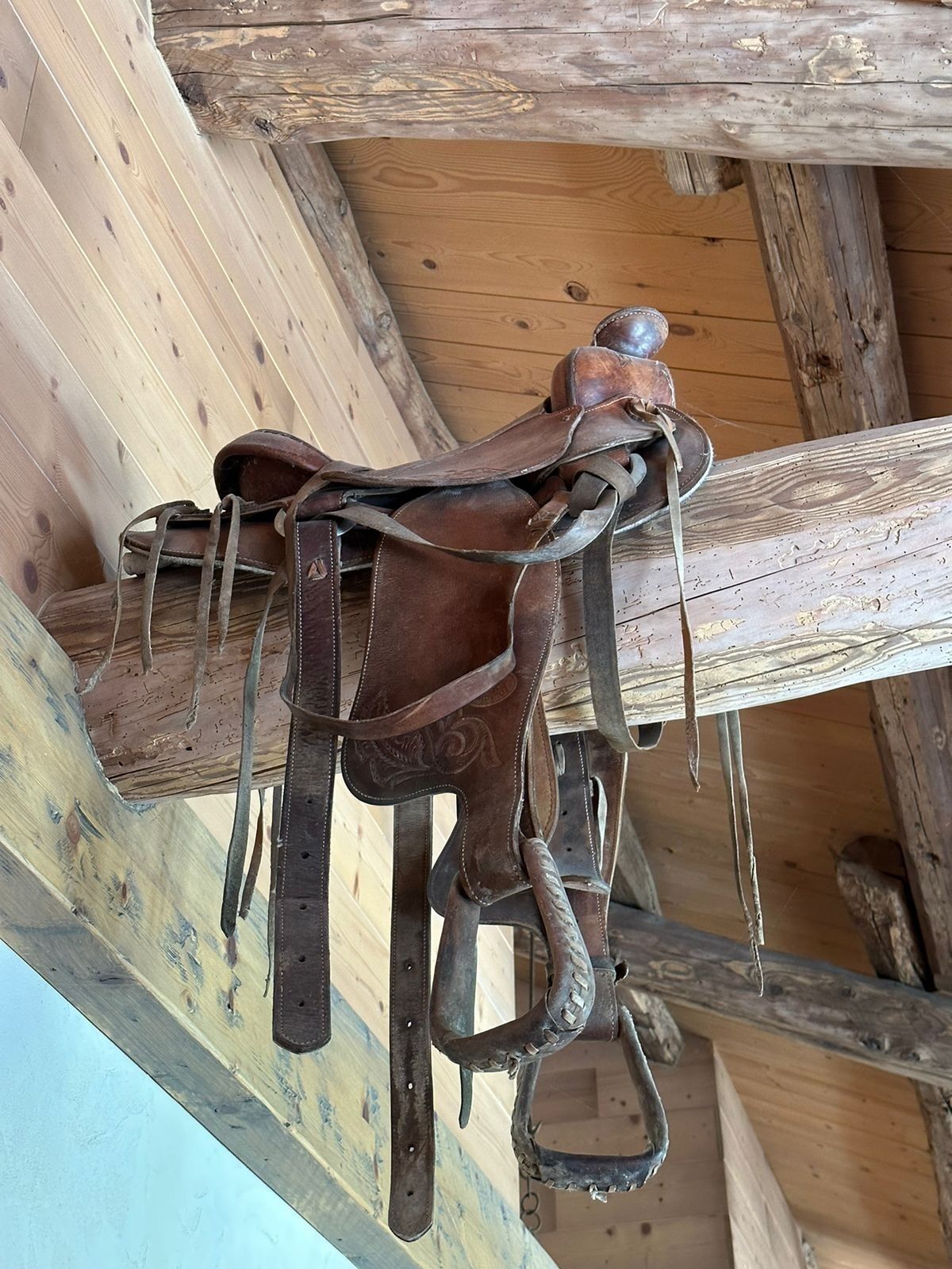 Un plafond en bois rustique, avec des poutres apparentes, et une selle en cuir suspendue.