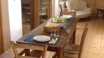 A dining area with a wooden table set for two, chairs, and a bowl of fruit.