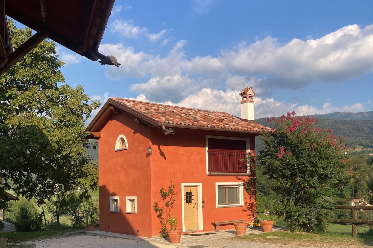 A red house with a tiled roof, a small porch, and a gravel driveway.