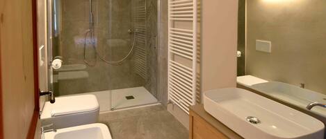 Un baño con ducha envuelta en cristal, un lavabo blanco y un tocador con espejo.
