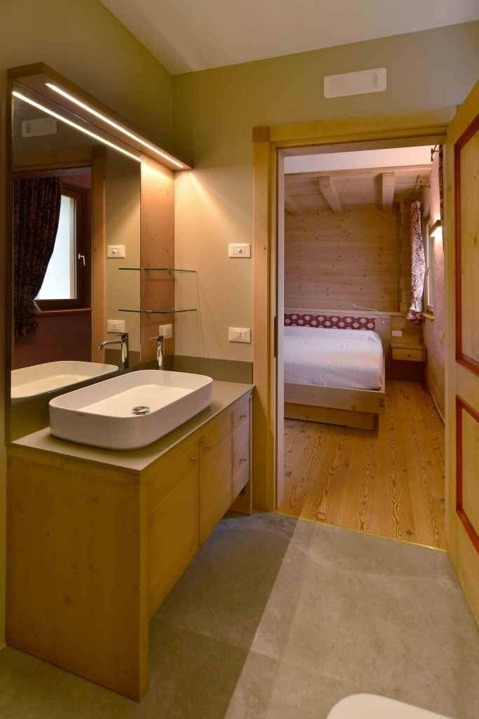 Una habitación con piso de madera, una cama con colcha estampada, un espejo grande y un lavamanos blanco.