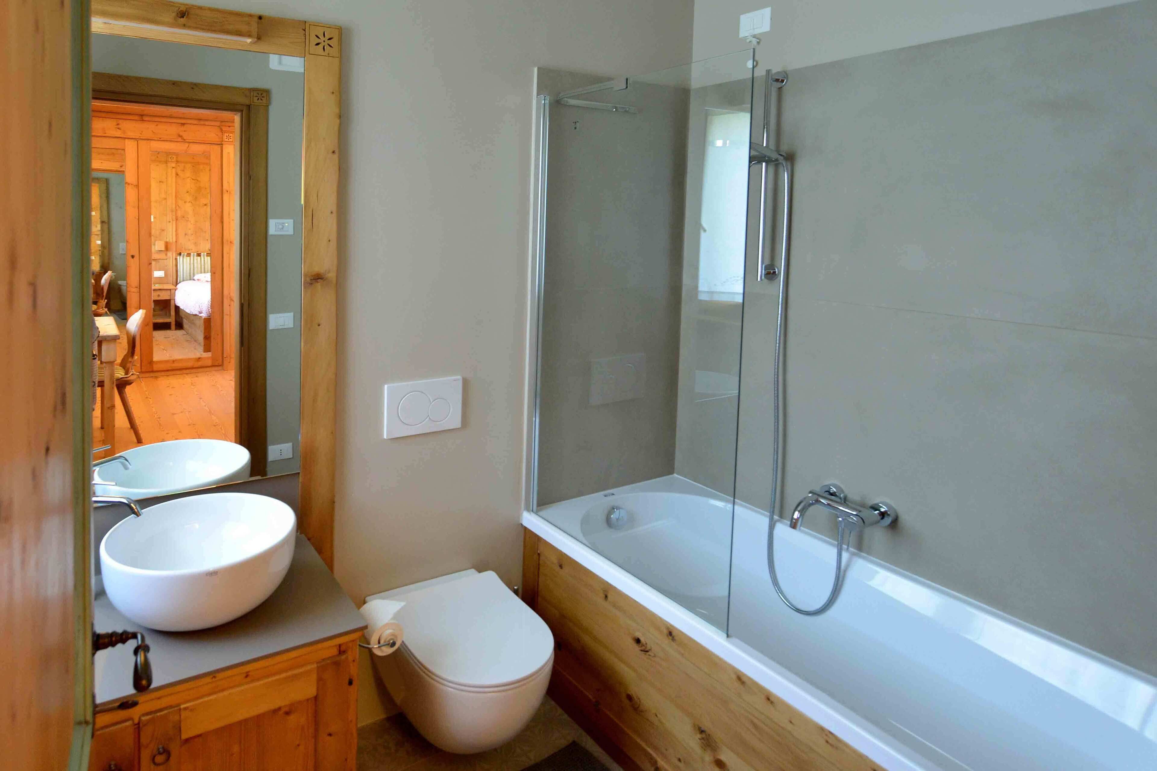 Een badkamer met een houten wastafel, een witte wasbak, een toilet en een douchecabine met bad.