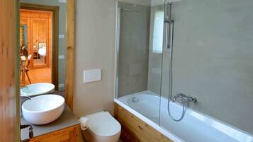 Een badkamer met een houten wastafel, een witte wasbak, een toilet en een douchecabine met bad.