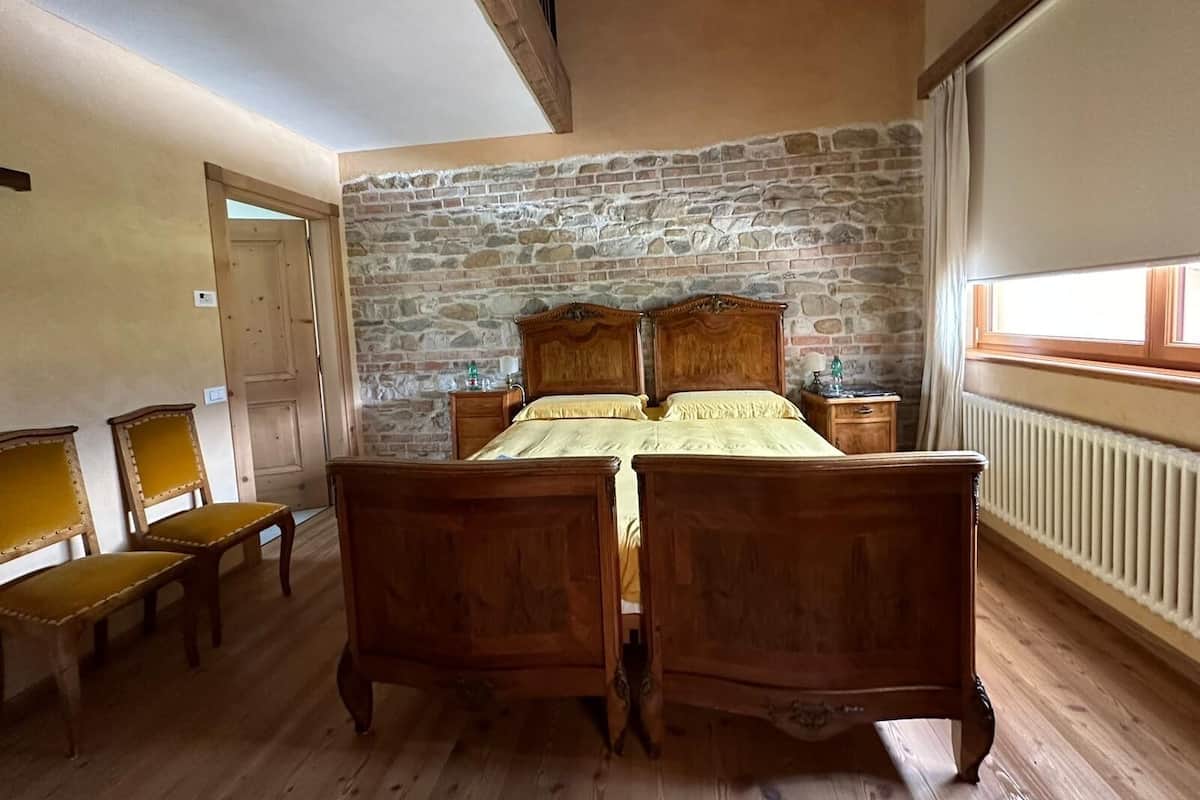 A bedroom with a stone wall, wooden bed, two bedside tables, a window, and a radiator.