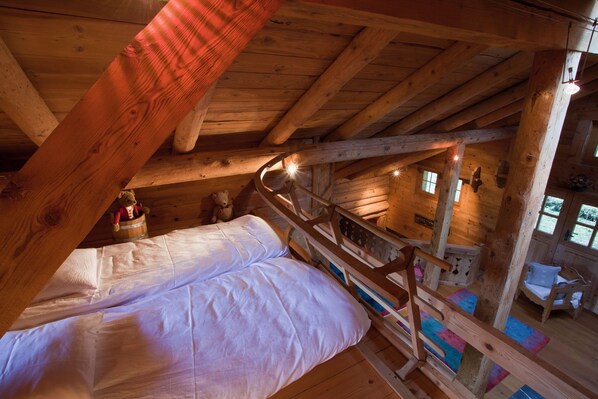 A wooden cabin with a loft bedroom featuring a bed, a wooden ladder, and a small seating area with a chair and a table. - Le Chalet de Lara (Val d'Illiez)