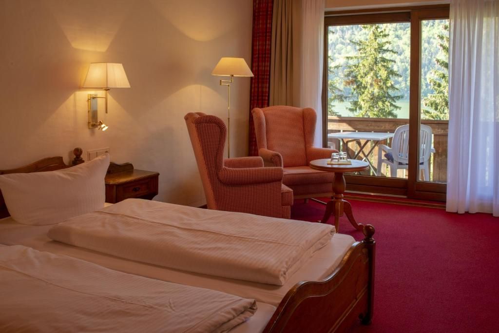 Ein Hotelzimmer mit einem Bett, einem Sessel, einem kleinen Tisch und Blick auf Bäume durch ein Fenster.