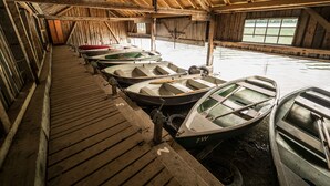 A covered boat storage area with several rowboats and canoes, wooden flooring, and a high ceiling with exposed beams. - Seehotel Weissensee (Fuessen)