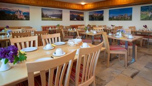A dining area with wooden tables and chairs, set with white plates, cups, and a vase of purple flowers. - Seehotel Weissensee (Fuessen)