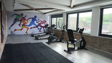 A gym with treadmills, an elliptical, and a stationary bike, with a mural of runners on the wall and large windows.