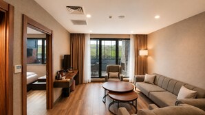 A hotel room with a sofa, a small table, a TV, and a balcony with a view. - Hilas Thermal Resort & Spa Aquapark (Ladik)
