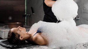 Une personne allongée sur une table de massage et recevant un soin de bain moussant.
