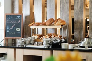 Un comptoir de boulangerie où sont exposés divers pains et pâtisseries, un tableau noir servant de menu et des plats de service.