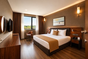 A hotel room with a large bed, a desk, a chair, a TV, and a painting on the wall.