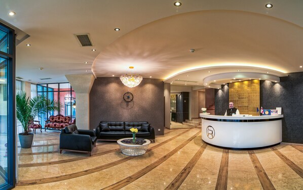 Eine moderne Hotelhalle mit einer Rezeption, Ledersofas, einem Chandelier und einer großen Pflanze.
