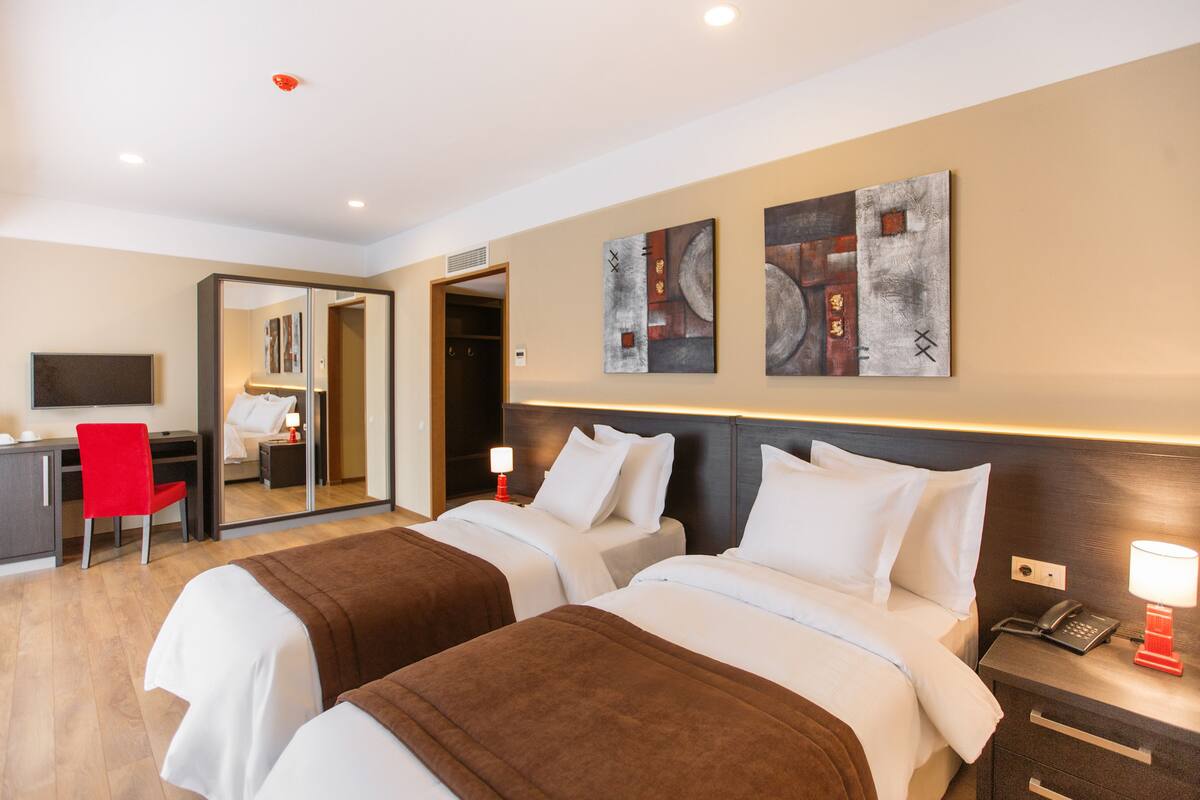 A hotel room with two beds, a desk, a chair, and artwork on the walls.