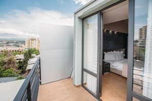 Ein modernes Schlafzimmer mit einer großen Schiebeglasdoor, die auf einen Balkon führt, einem Bett mit weißen Bettbezügen und Blick auf die Stadtlandschaft.