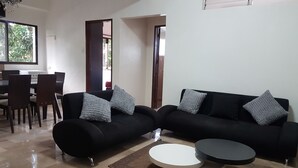 Un salon moderne avec un canapé noir, deux petites tables basses rondes blanches et un lustre.