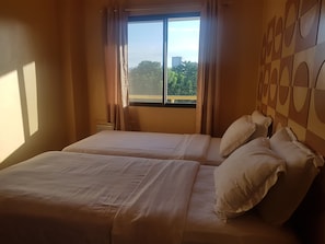 Habitació d'hotel amb dos llits, una finestra gran amb cortines, i vista a la ciutat.