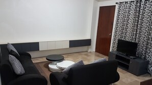 Un salon moderne avec un canapé noir, une table basse ronde, un téléviseur à écran plat et un rideau à motifs.