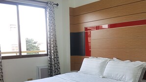 Une chambre avec un grand lit, une fenêtre avec des rideaux, un radiateur et une tête de lit en bois avec une touche de couleur rouge.
