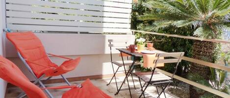A balcony with two orange chairs, a small table, and a potted plant.