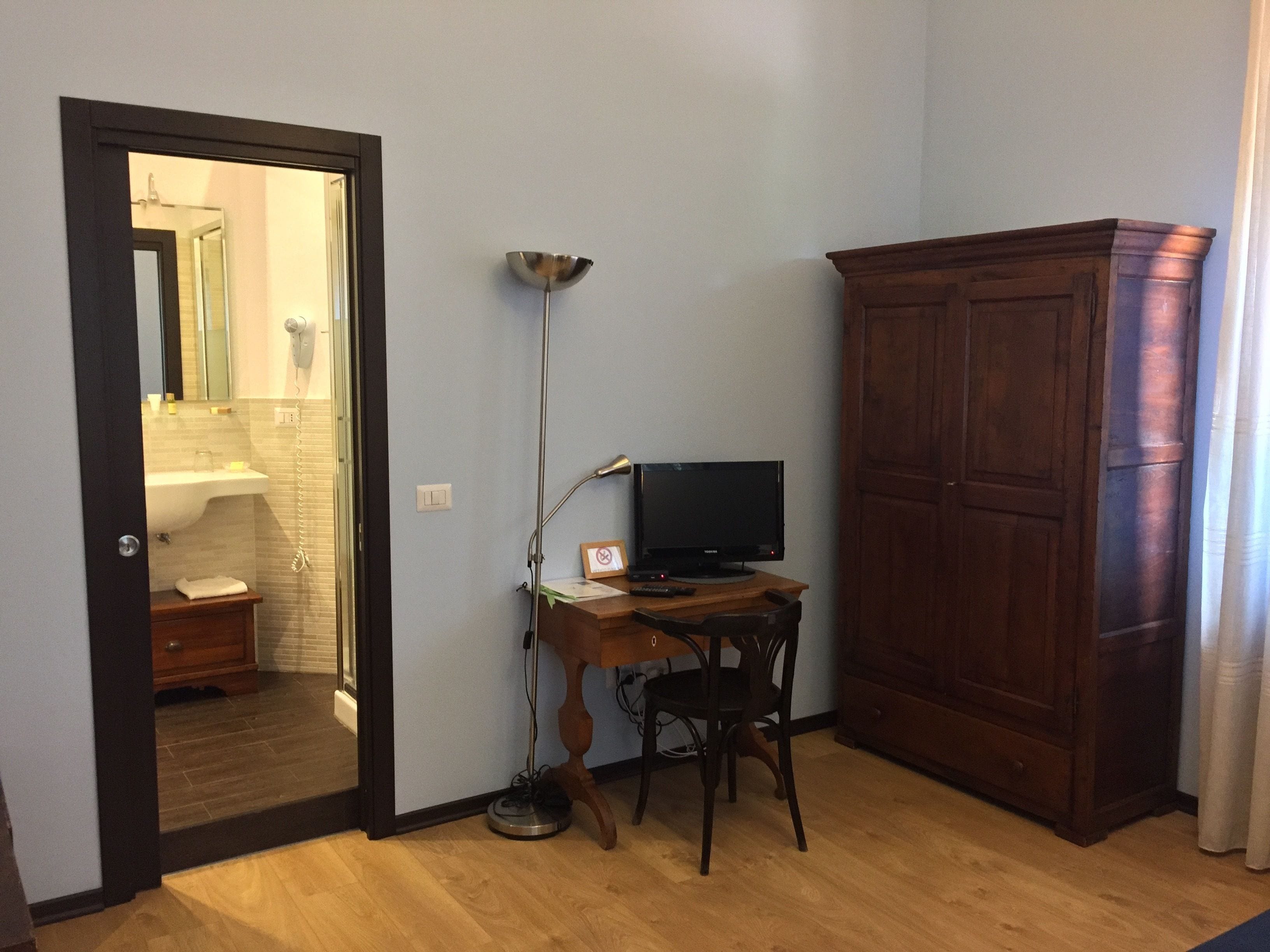 A room with a wooden cabinet, a desk with a computer, a standing lamp, and a mirror.
