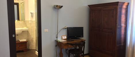 A room with a wooden cabinet, a desk with a computer, a standing lamp, and a mirror.