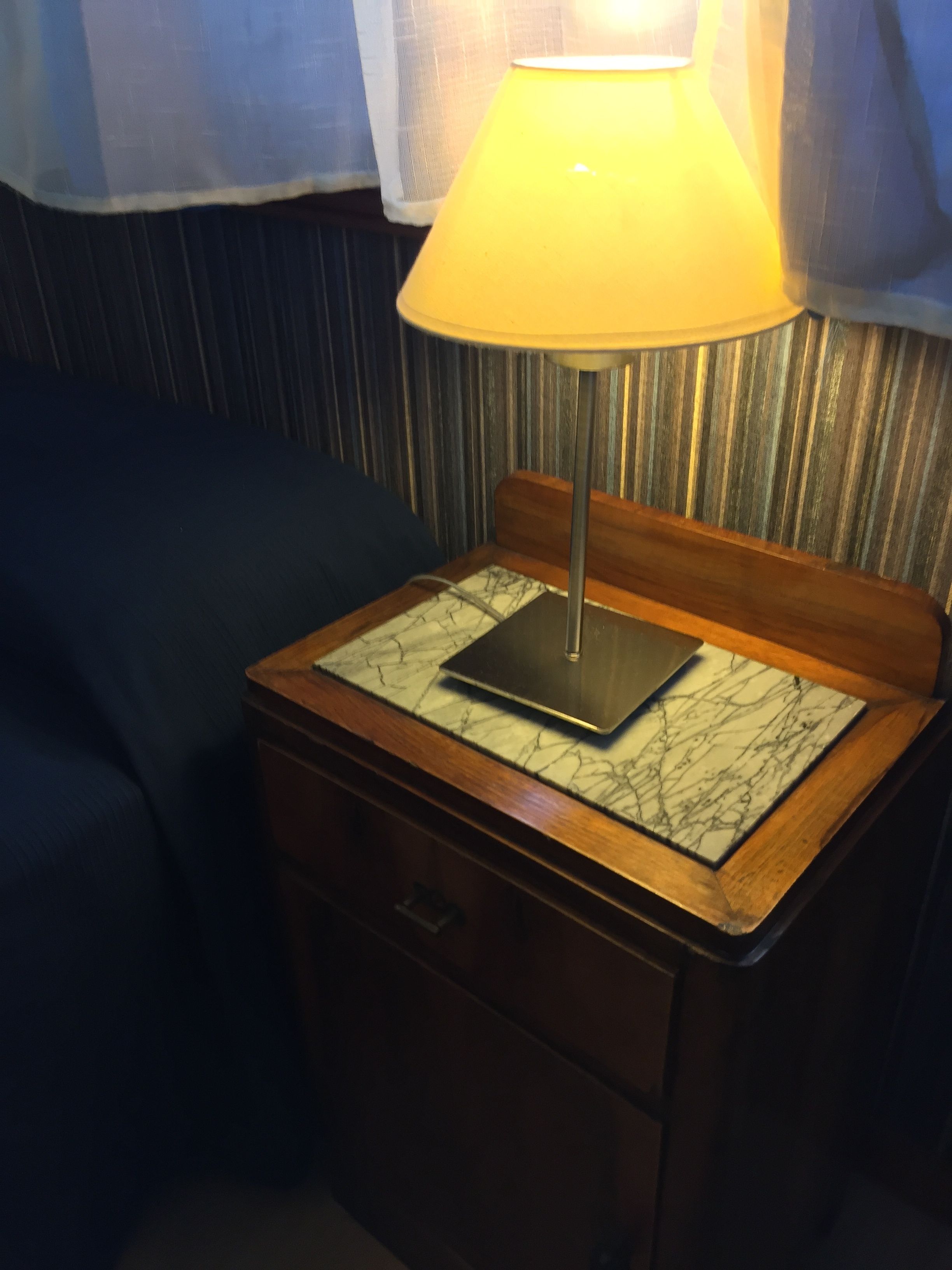 A bedside table with a lamp, a book, and a drawer.