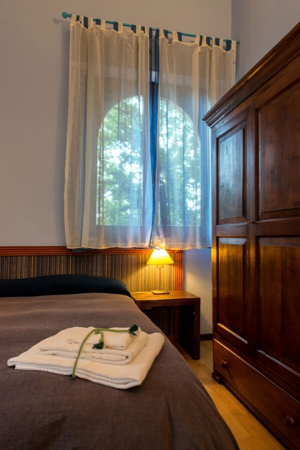 A hotel room with a bed, a wooden wardrobe, a window with sheer curtains, and a bedside lamp. - B&B Domus Verdiana (Ragalna)