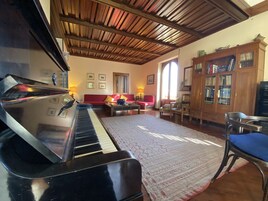 Un salón con un piano de cola, un sofá rojo, un aparador de madera con puertas de cristal y una alfombra estampada.