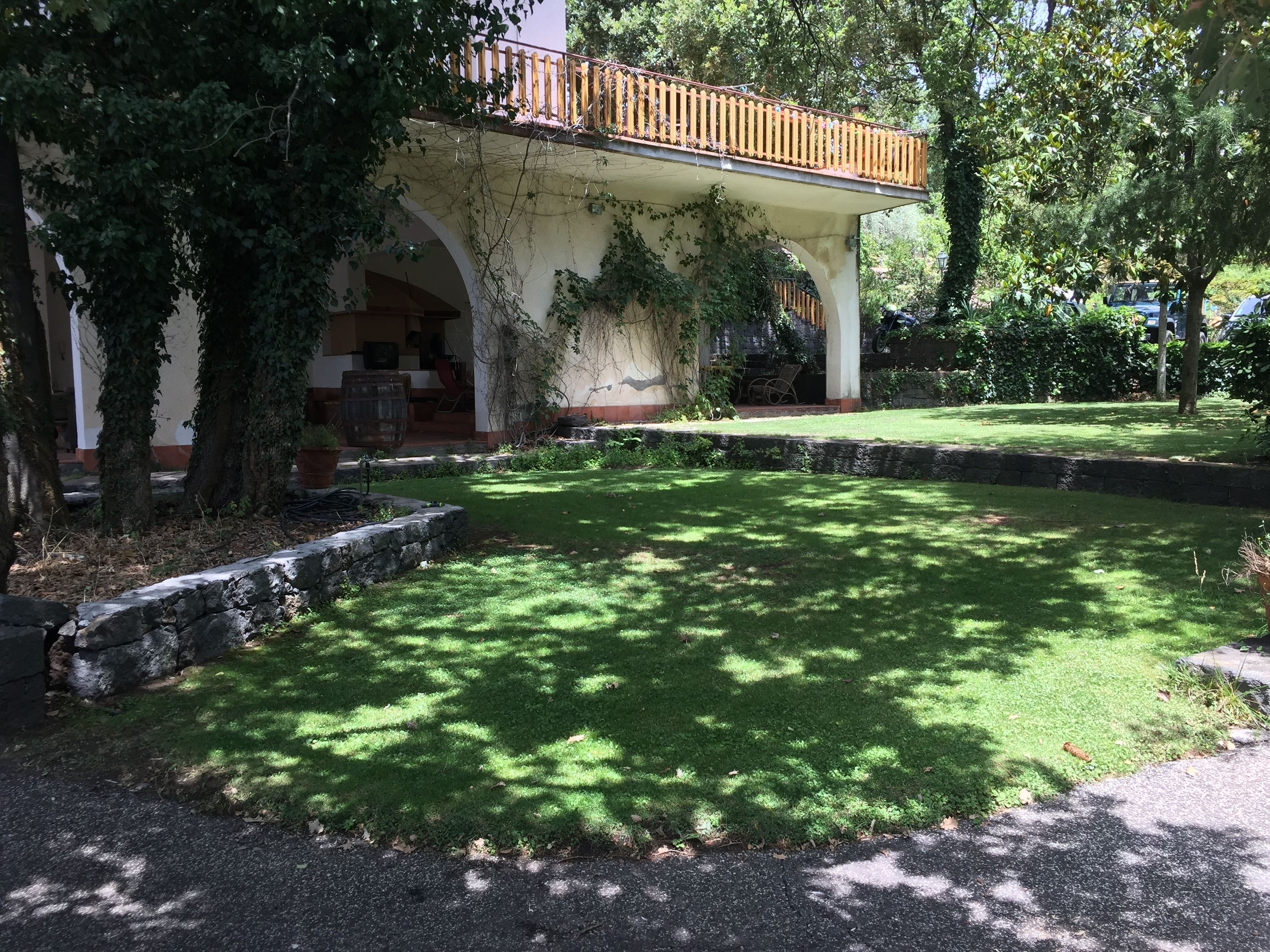 A covered patio area with a stone retaining wall, a grassy lawn, and a wooden fence.