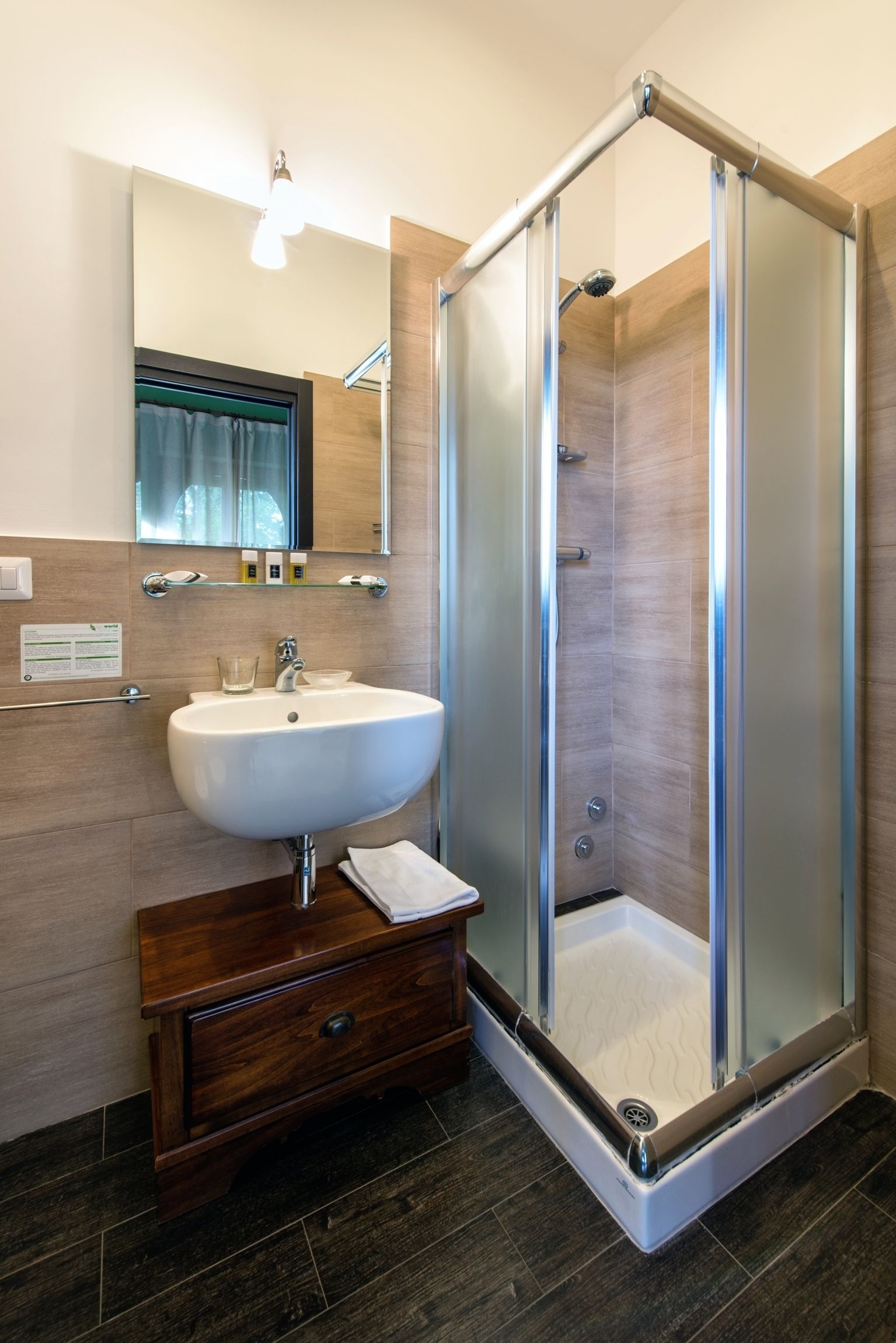 Een moderne badkamer met een douchecabine van glas, een wit wastafelmeubel en een houten opbergkast.