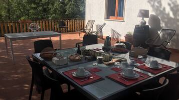 Un coin repas avec une table dressée pour deux personnes, entourée de chaises, d’une fenêtre et d’une lampe.