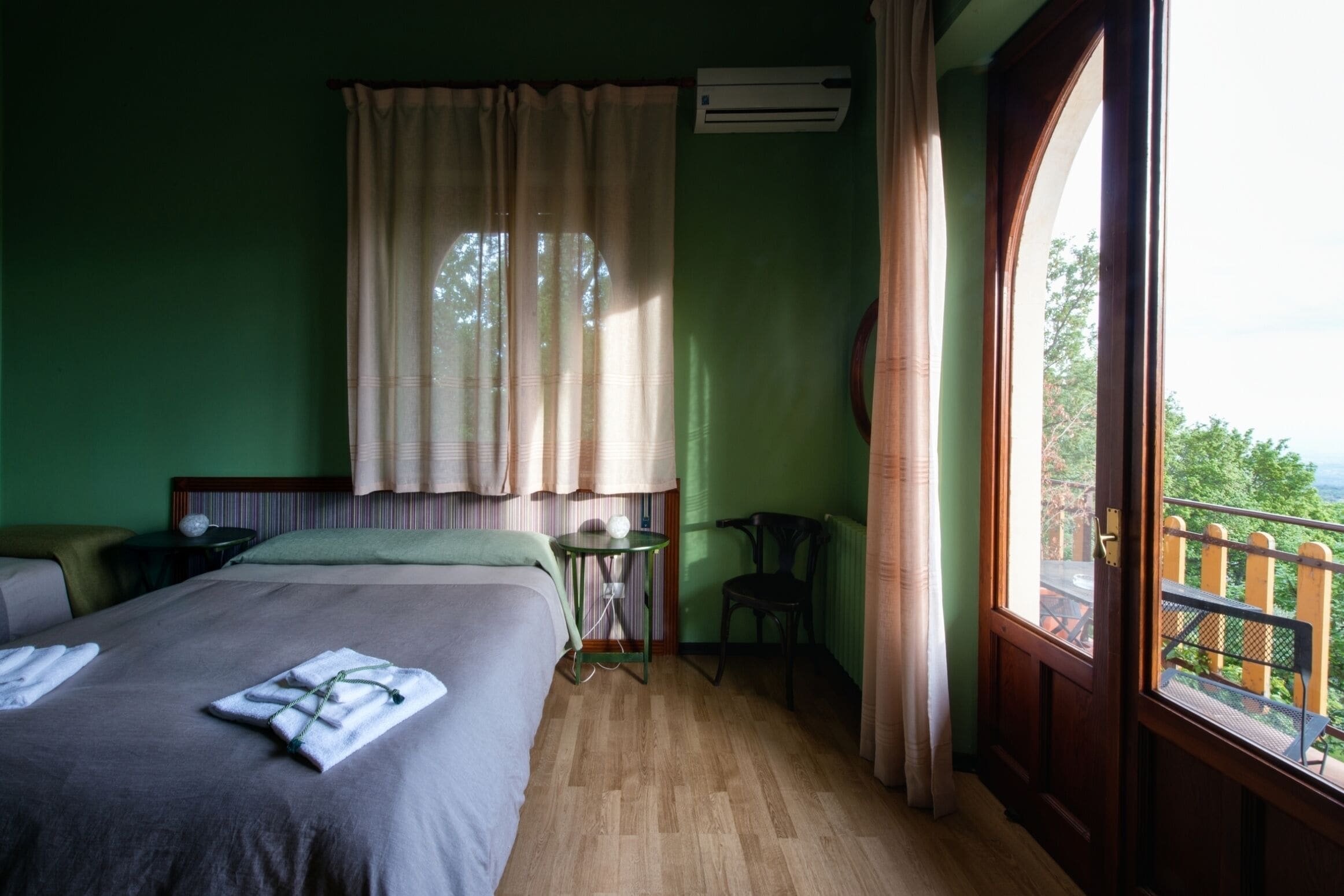 A hotel room with a bed, a small table, a chair, and a view of the outdoors.