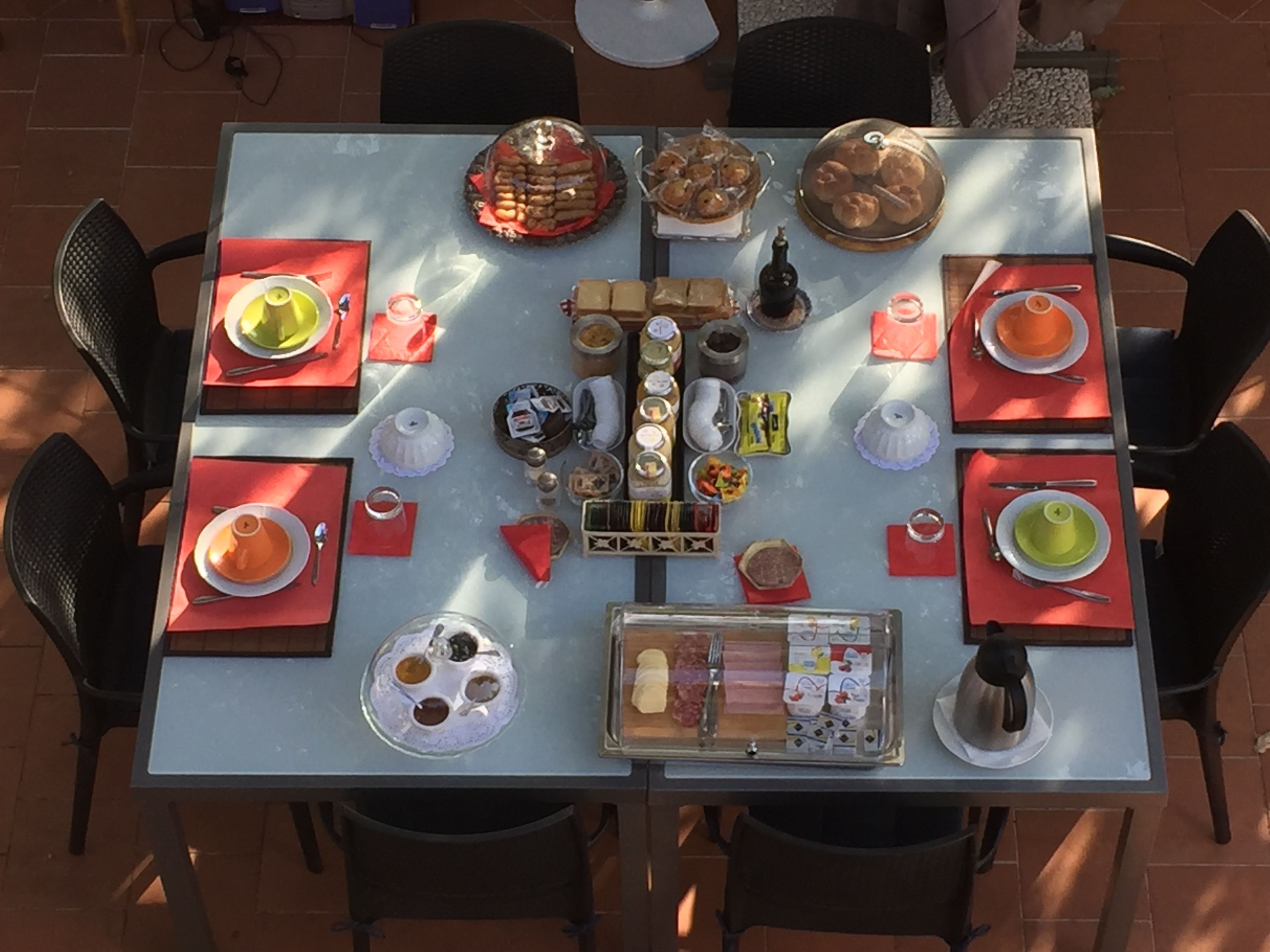 A table set for a meal with various dishes, including pastries and condiments, in an outdoor setting with chairs around.
