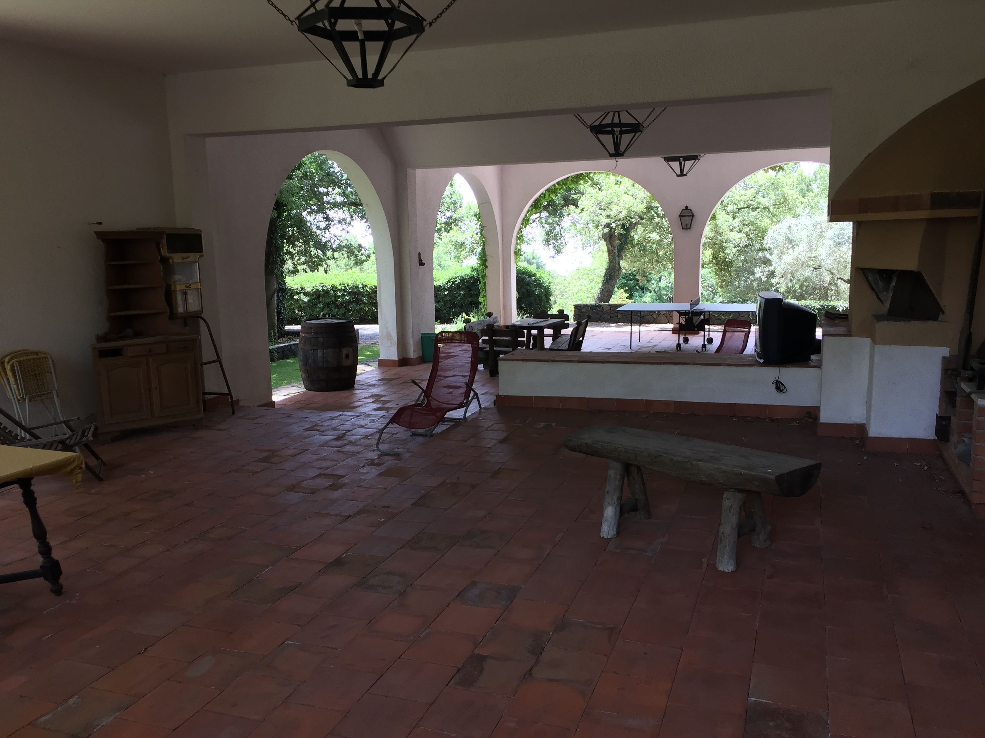 An open patio with a tiled floor, a wooden bench, a red folding chair, a table, and a stone barrel.