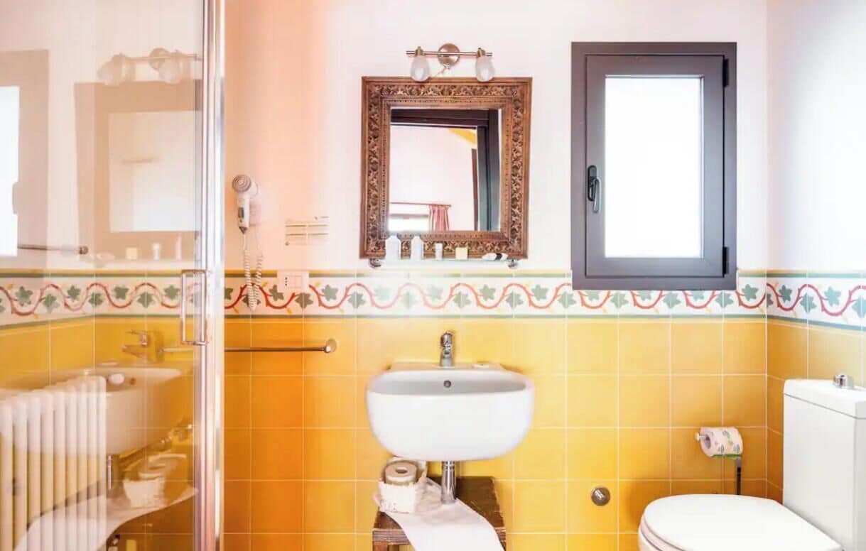 A bathroom with a yellow tiled wall, a white sink, a mirror, and a toilet.