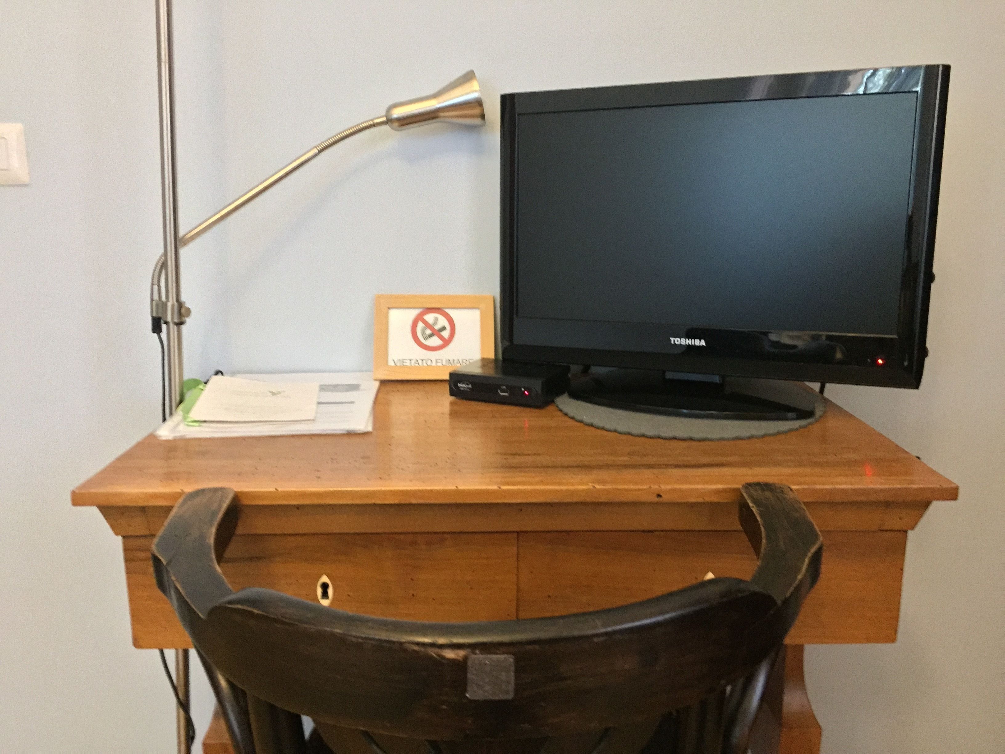 A wooden desk with a black monitor, a lamp, and a chair.