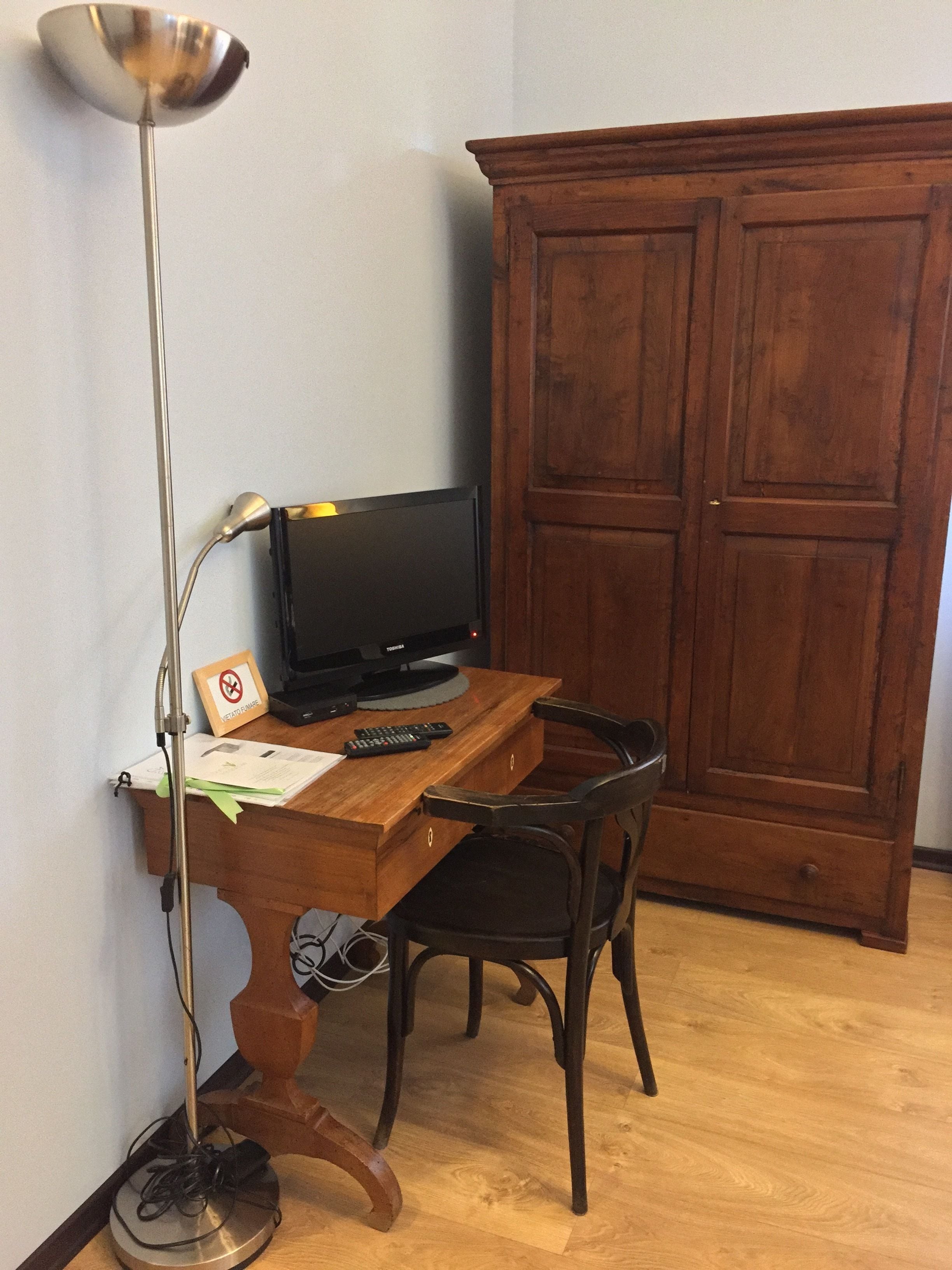 Ett skrivbord i trä med en tv, en stol, en golvlampa och ett skåp.