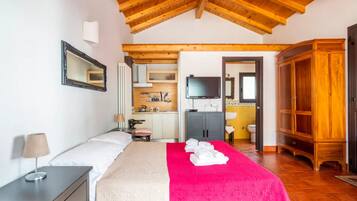 Quarto com cama, mesa de cabeceira, televisão, guarda-roupa de madeira e banheiro visível através de uma porta aberta.