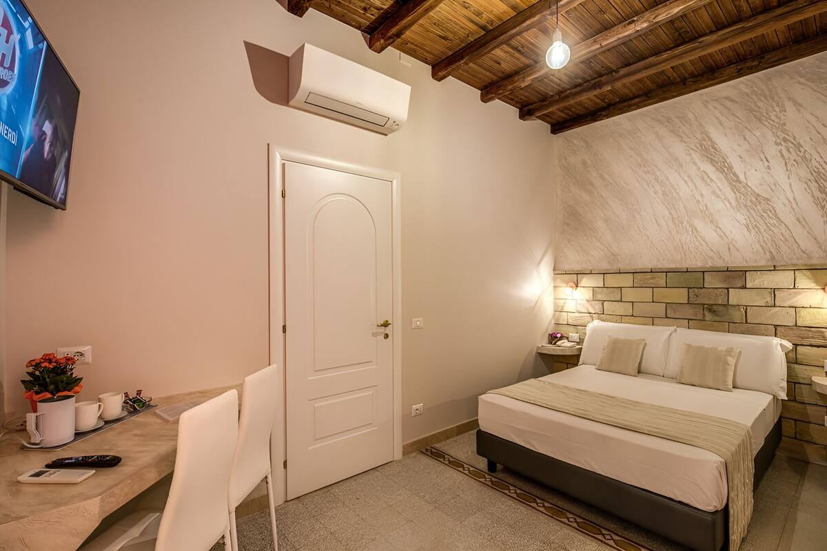 A bedroom with a bed, bedside table, and a TV mounted on the wall.