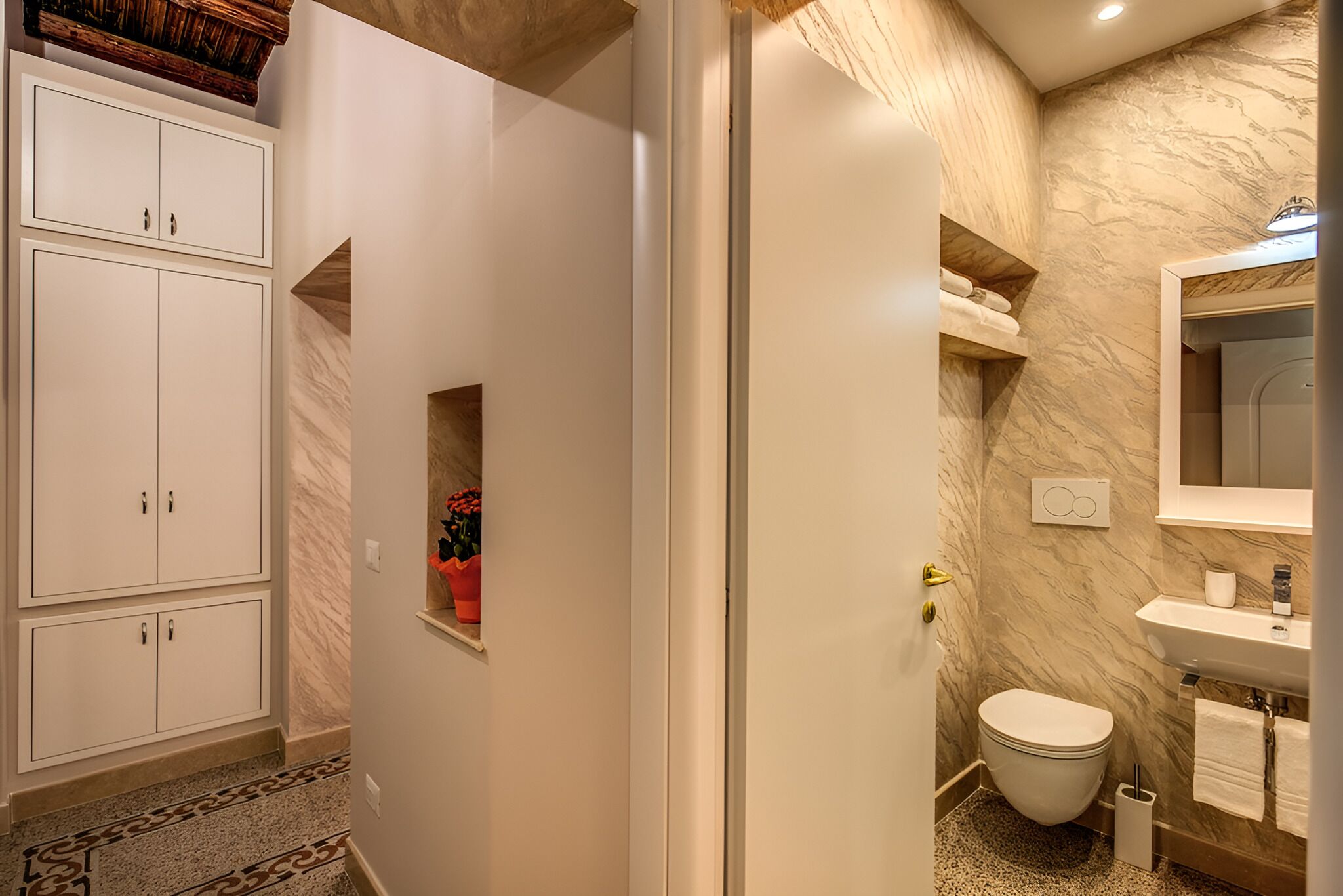 A bathroom with a marble wall, a white toilet, a sink, and a cabinet with a towel shelf.
