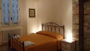 Ein Schlafzimmer mit Bett, Nachttisch, Heizkörper, Kamin und einem Fenster mit Vorhängen.