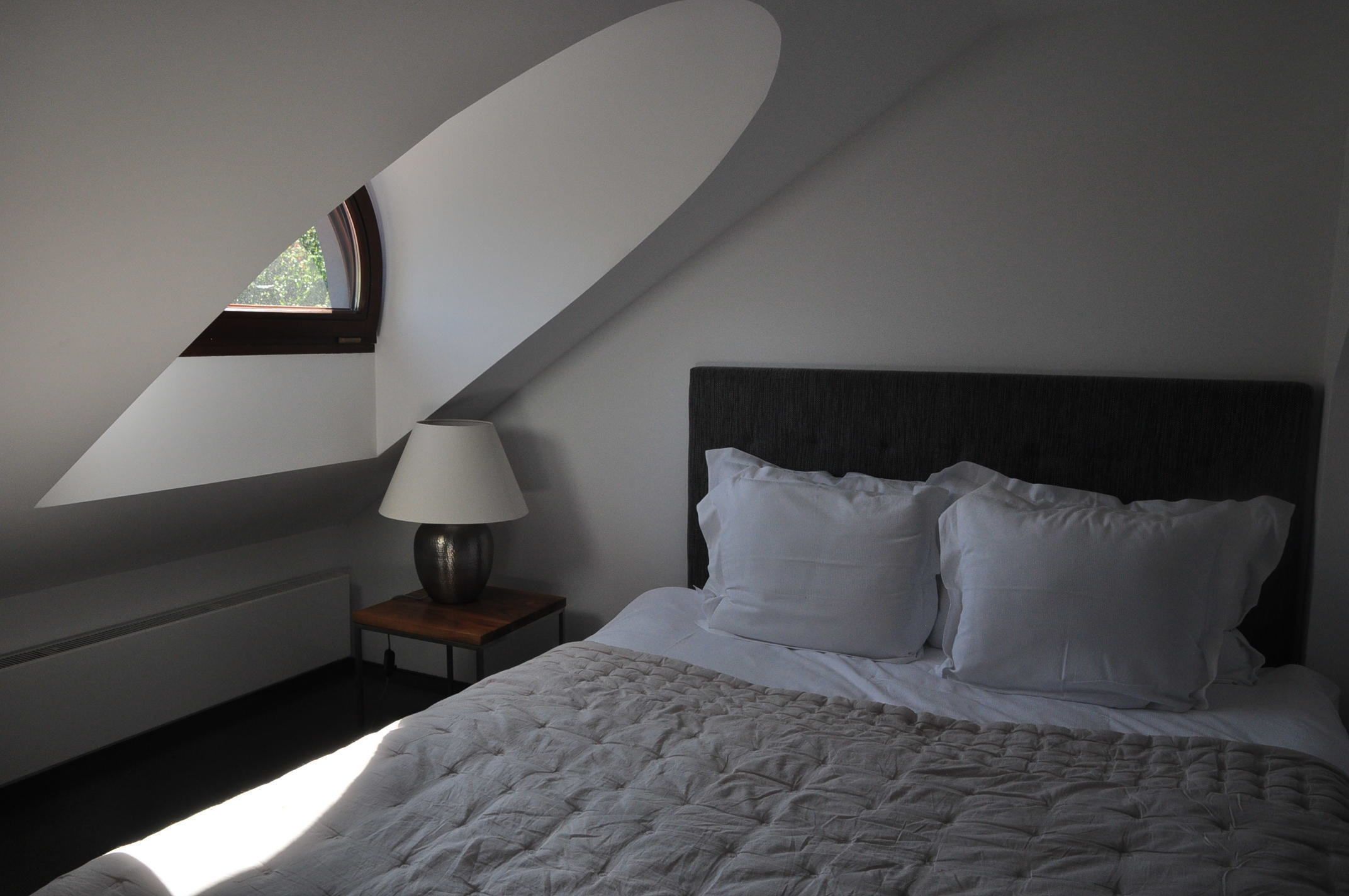 A bedroom with a bed, a nightstand, a lamp, and a window.