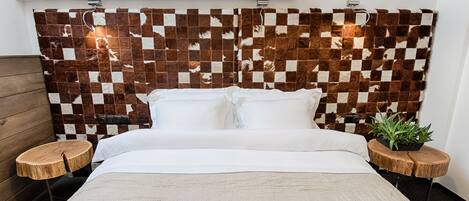 A bed with white linens, a checkered fur headboard, and two wooden nightstands with plants.