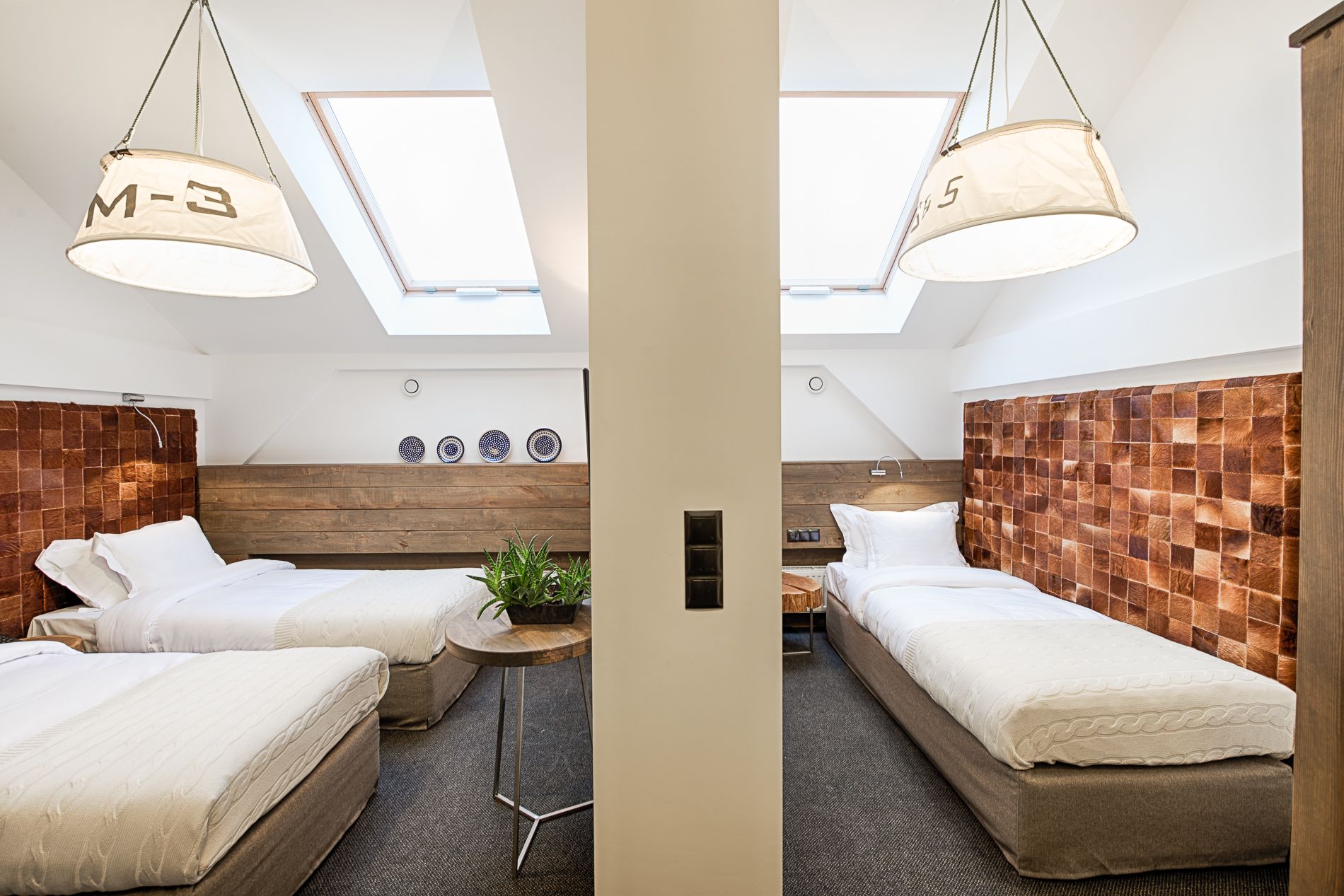 Habitación de hotel moderna con dos camas, tragaluz, cabecero de madera y una planta pequeña.