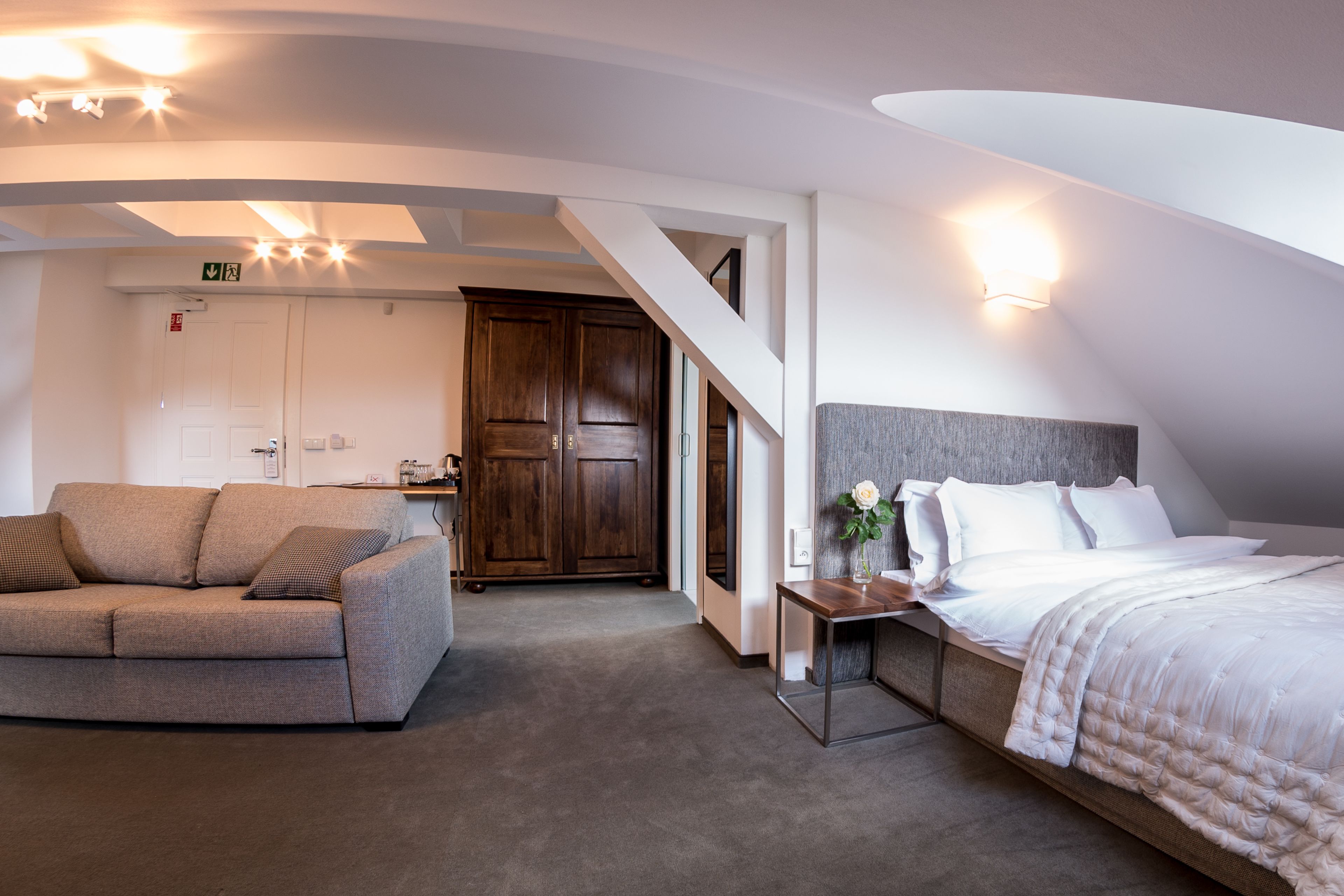A modern hotel room with a sofa, a bed with a large window, and a staircase leading to another level.
