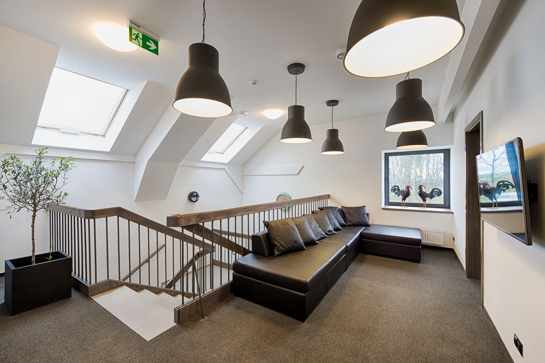 Un interior moderno con una escalera de madera, un sofá de cuero negro e iluminación colgante.